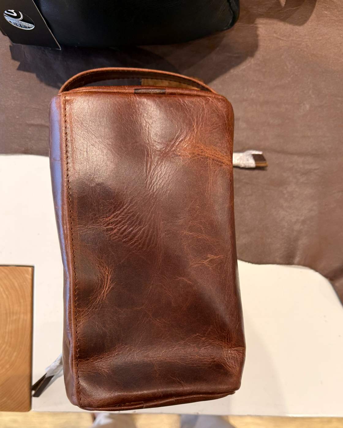 Real photo of the plain back panel of the dopp kit, showing the crease marks and lighter pull-up areas of the crazy-horse leather.