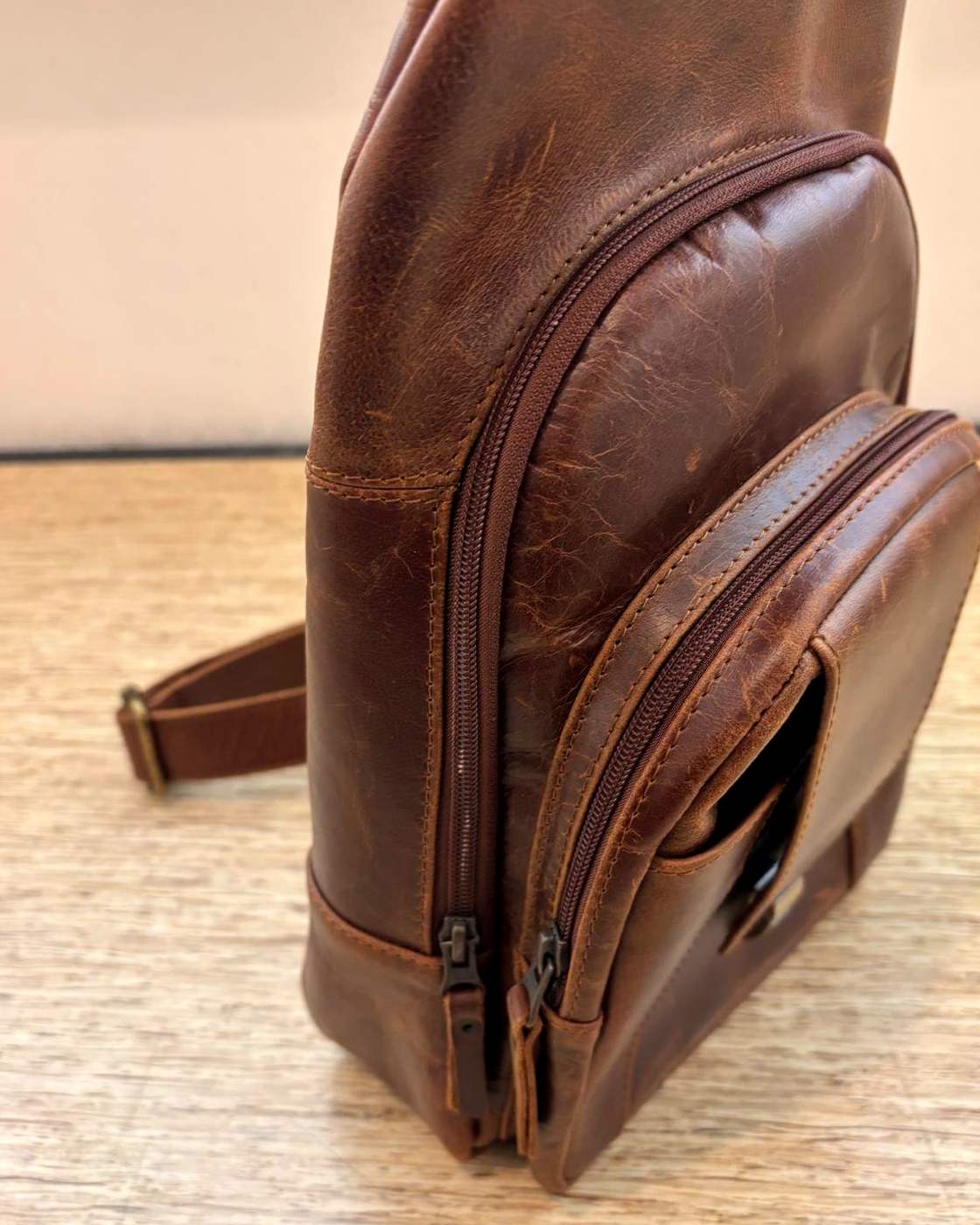 Real photo of the Courier Sling from the front corner, showing the two zips on the front of the bag with their pulls at the bottom, the seam between the main compartment and the front pocket, and the open slot pocket on the side.