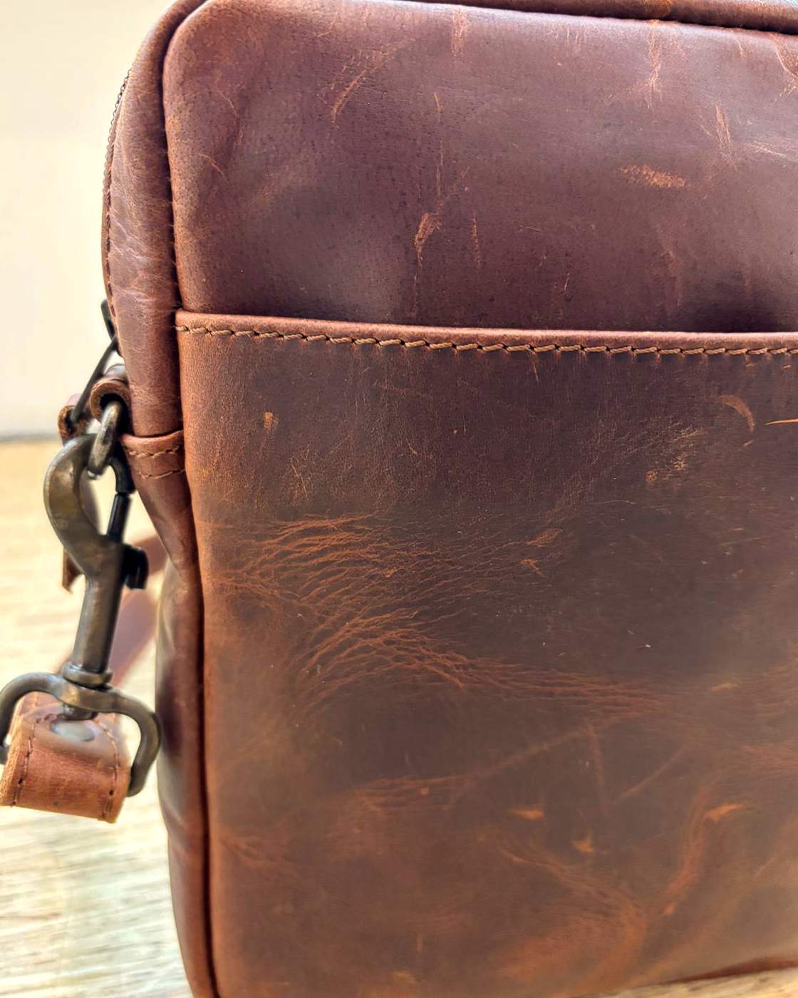 Close-up real photo of the YYZ Satchel leather and stitching at the top corner, showing the grain, the marks in the hide and the stitched top edge of the slip pocket.