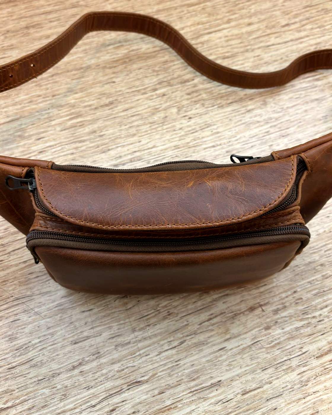 Close real photo of the front of the Nomad Sling, showing the zipped front pocket with its curved top edge sitting over the main zip that runs along the top of the body.