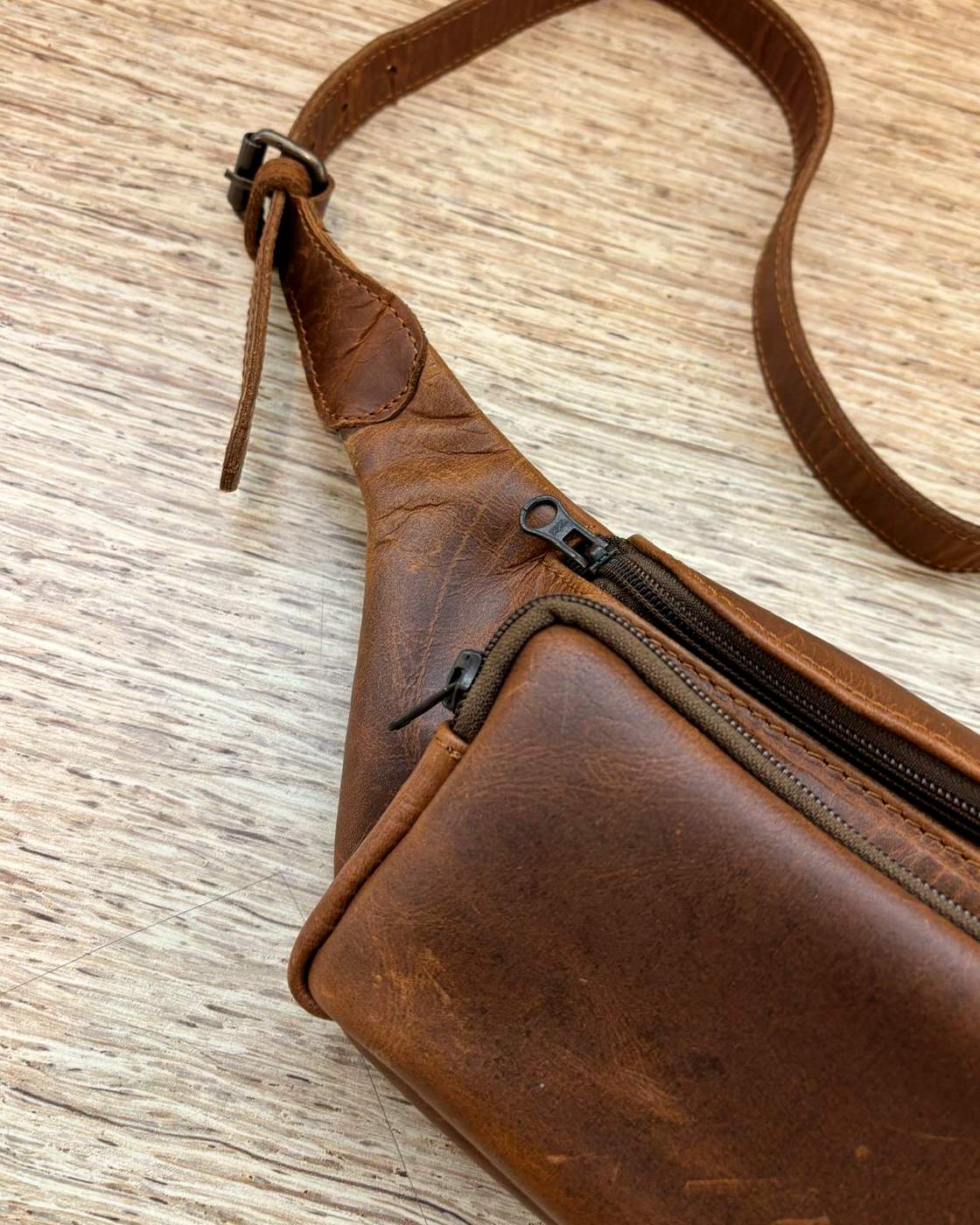 Real photo of the Nomad Sling shot from above at an angle, showing the two separate zips and their pulls, the front pocket, and the strap running off the top of the frame.