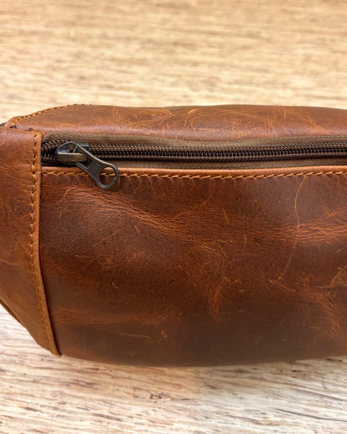 Close-up real photo of a zip on the Nomad Sling, showing the zip teeth, the tape, the metal pull and the grain and stitching of the leather around it.