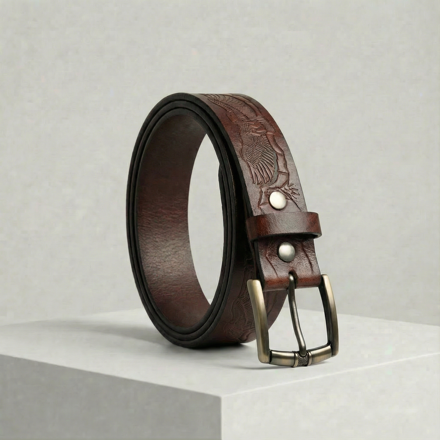 Bellvari Ironhide full-grain leather belt with hand-tooled floral pattern and antique-brass buckle on a neutral background.