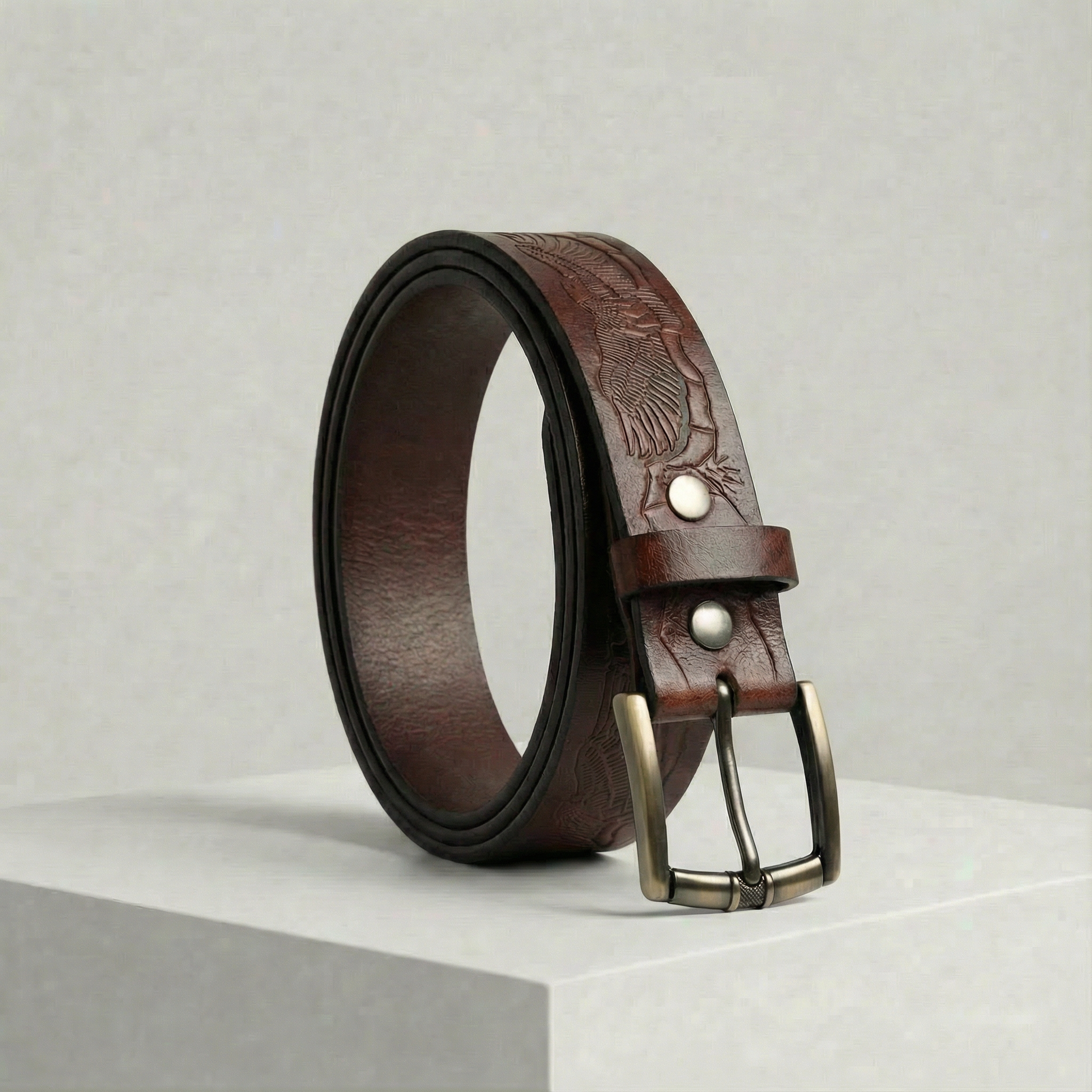 Bellvari Ironhide full-grain leather belt with hand-tooled floral pattern and antique-brass buckle on a neutral background.