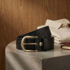 Bellvari Ironhide black leather belt coiled, showing the tooled relief and brass hardware. — view 7