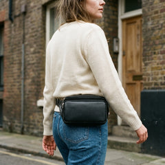 A woman wearing the Bellvari Nomad Sling at her waist in black full-grain leather, on a city street. — view 14