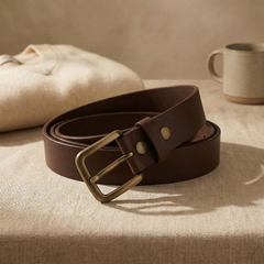 Bellvari Tradesman brown full-grain leather belt coiled on linen, showing the grain, brass buckle. — view 4