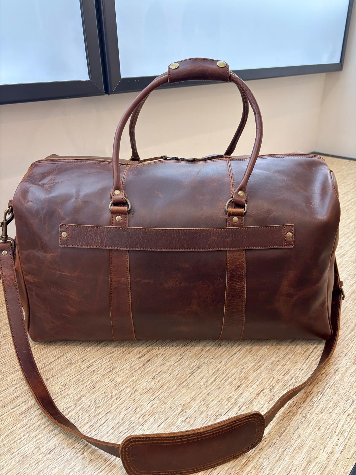 The Crazy Horse Brown Weekender on a wooden table, showing the rear trolley sleeve, handles and shoulder strap.
