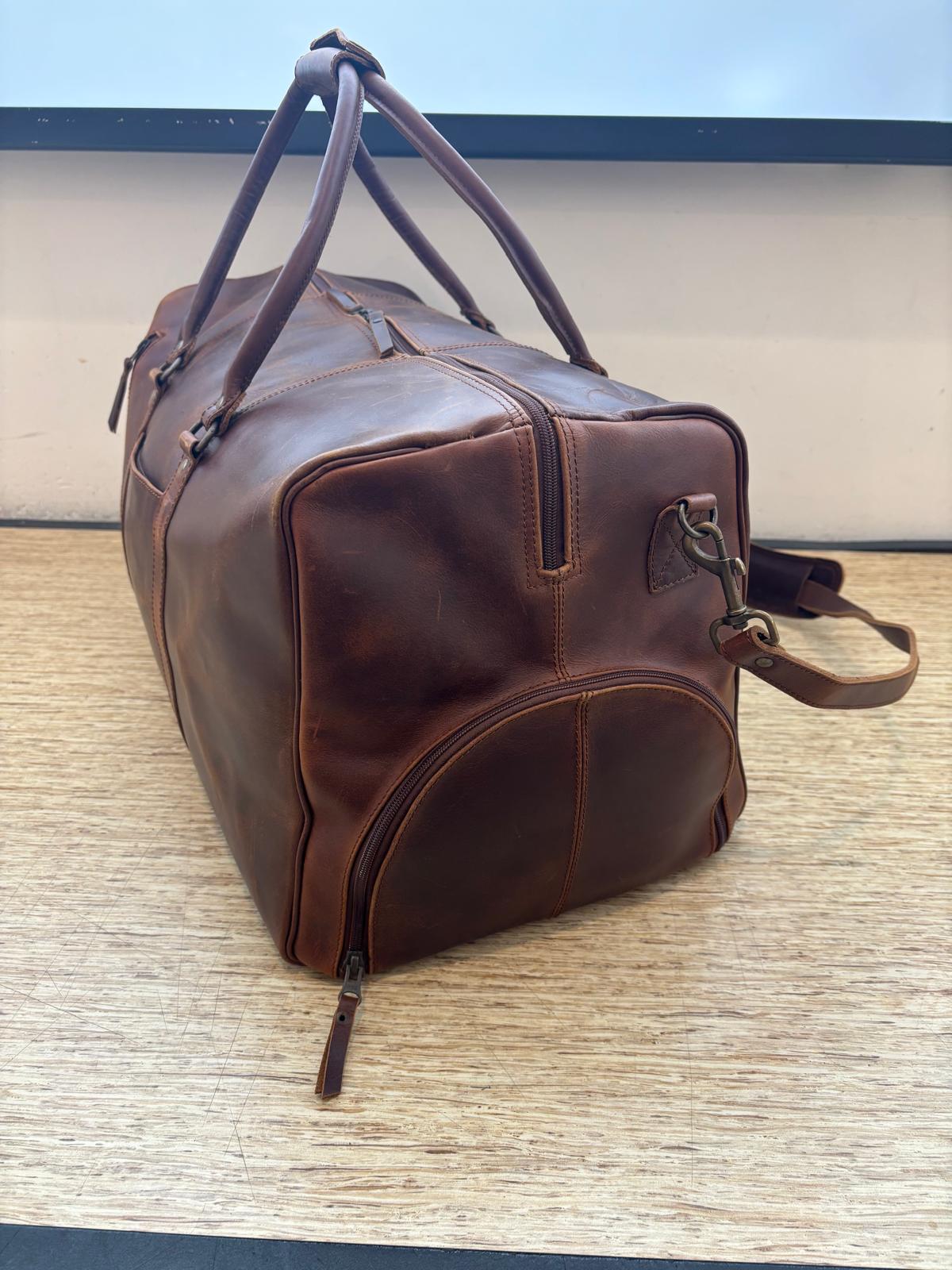 The Crazy Horse Brown Weekender on a wooden table, showing the side zipper and shoulder strap hook.