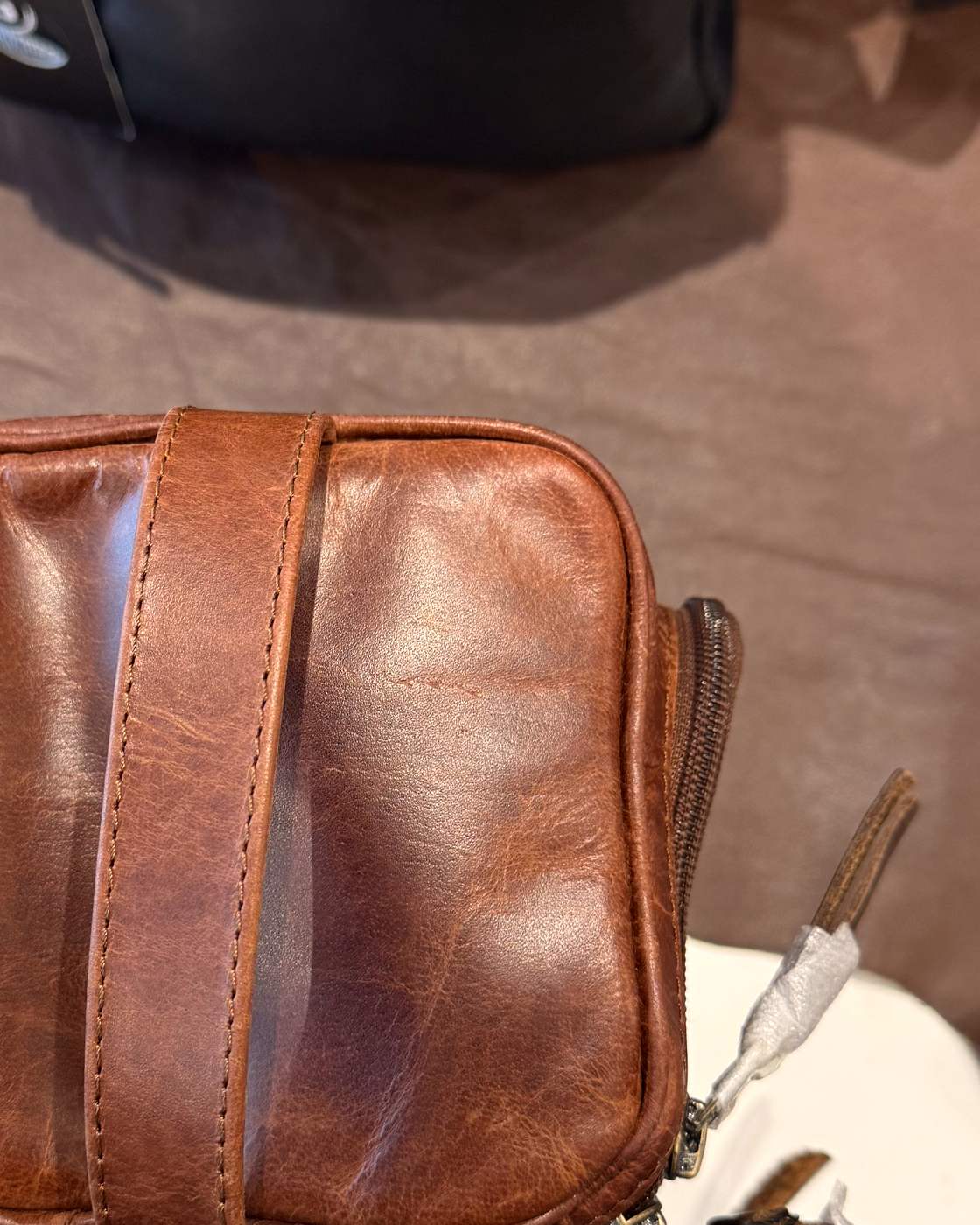 Real photo of the end of the dopp kit, showing the flat leather handle stitched vertically across the end panel.
