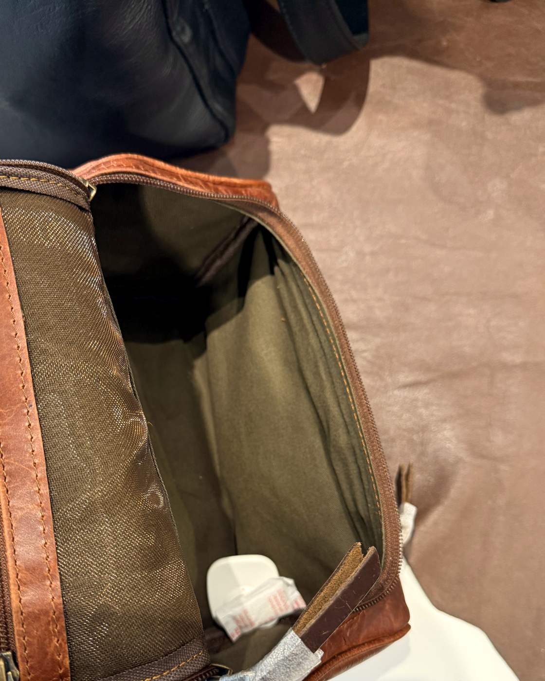 Real photo looking along the open dopp kit, showing the mesh zip pocket inside the lid with its leather trim, the brass D-ring, and the depth of the main compartment.