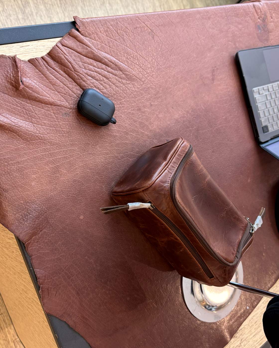 Real photo from above of the dopp kit on a leather hide on the shop counter with an AirPods case beside it for scale.