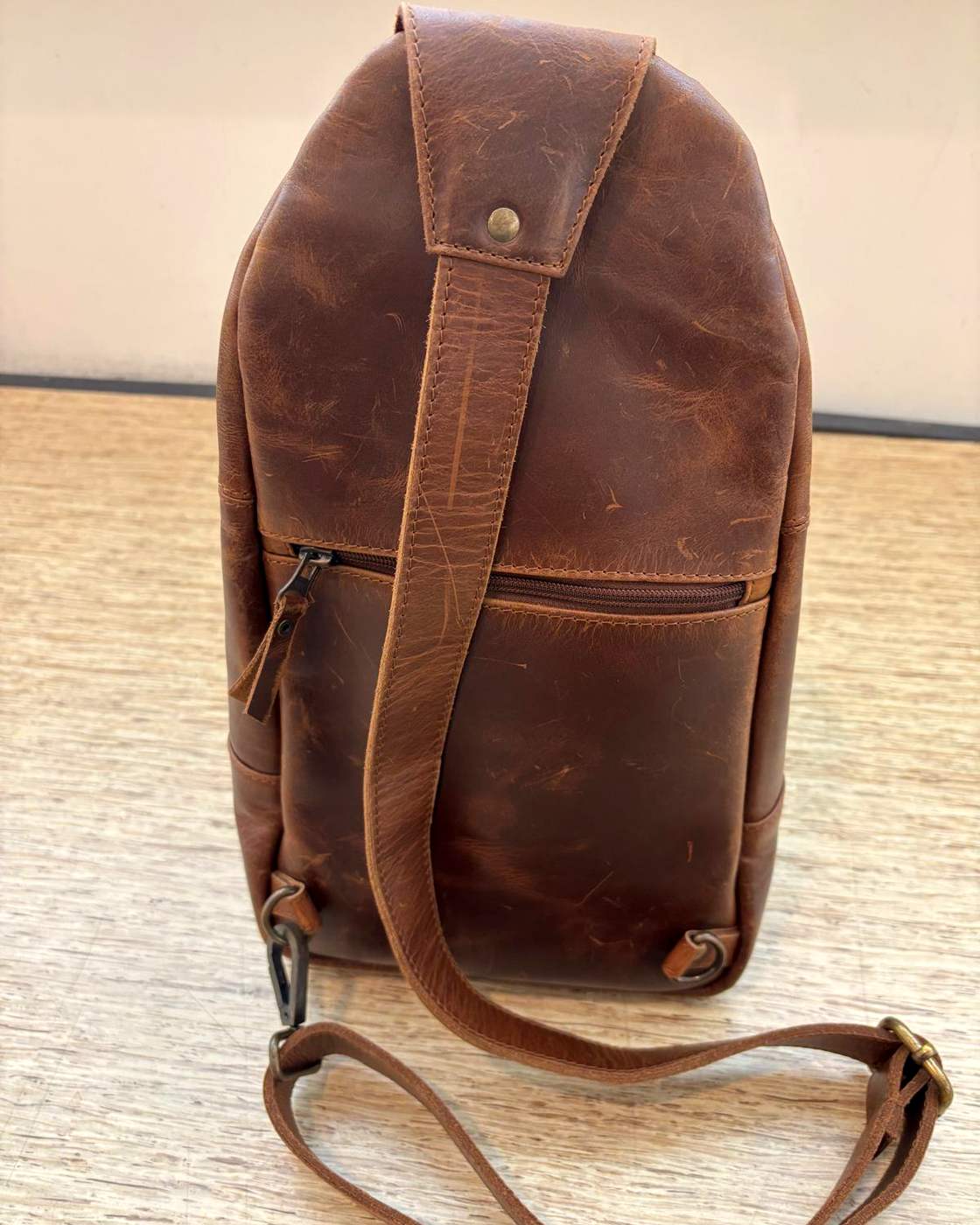 Real photo of the Courier Sling from behind, showing the wide strap panel down the centre of the back, the zipped pocket across the back, the clip points at the bottom corners and the adjustable strap laid out on the table.