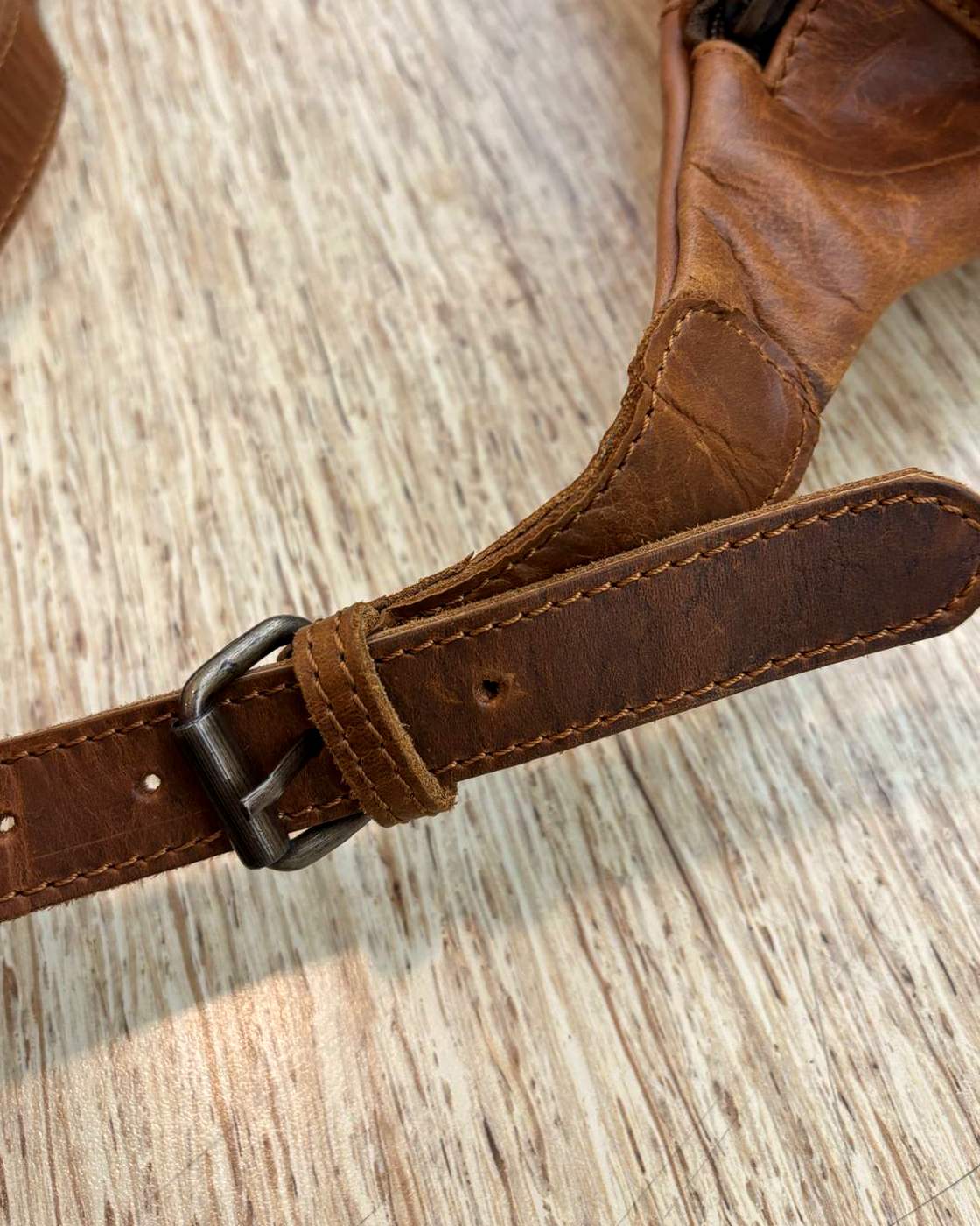 Close-up real photo of the adjuster on the Nomad Sling strap, showing the metal hardware that sets the strap length and the stitched leather strap running through it.
